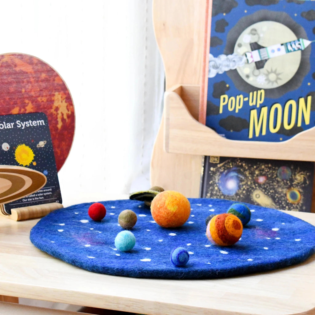Children's educational toys including a solar system model and a pop-up moon book on a wooden surface.