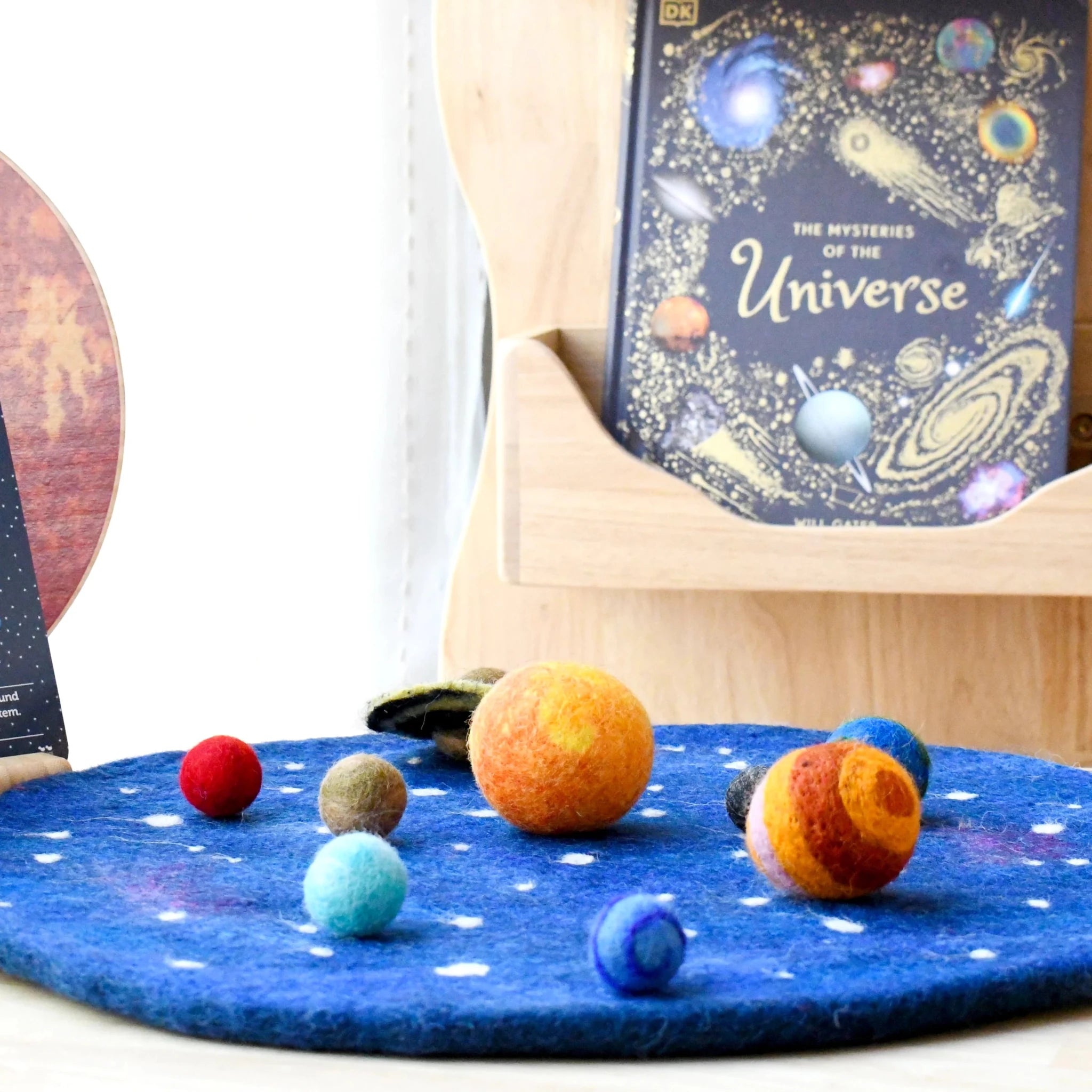 Model of planets on a blue surface with a book titled 'The Mysteries of the Universe' in the background.