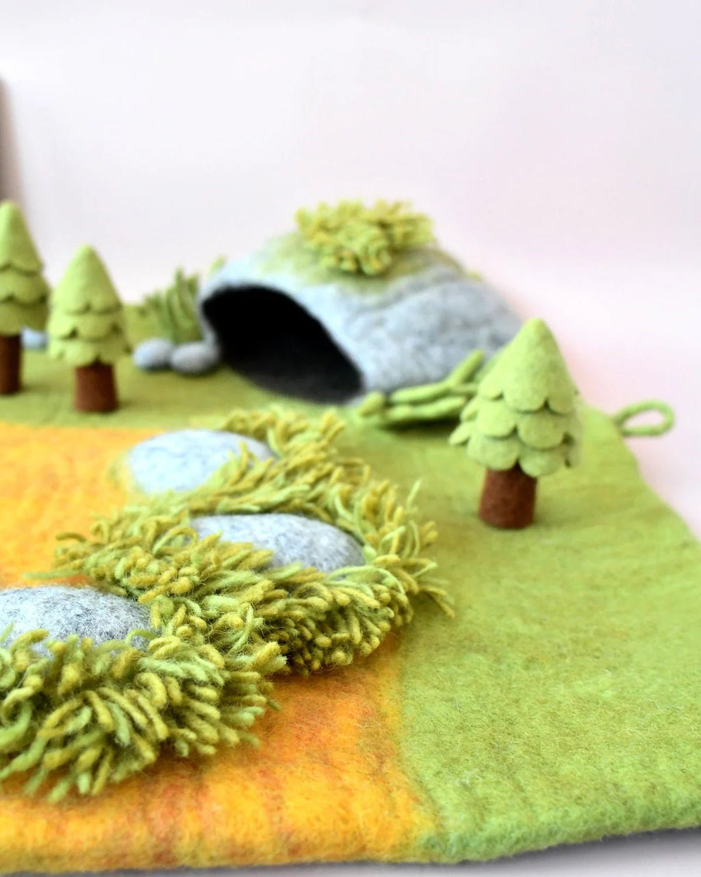 Felt landscape with trees, rocks, and a cave on a green background