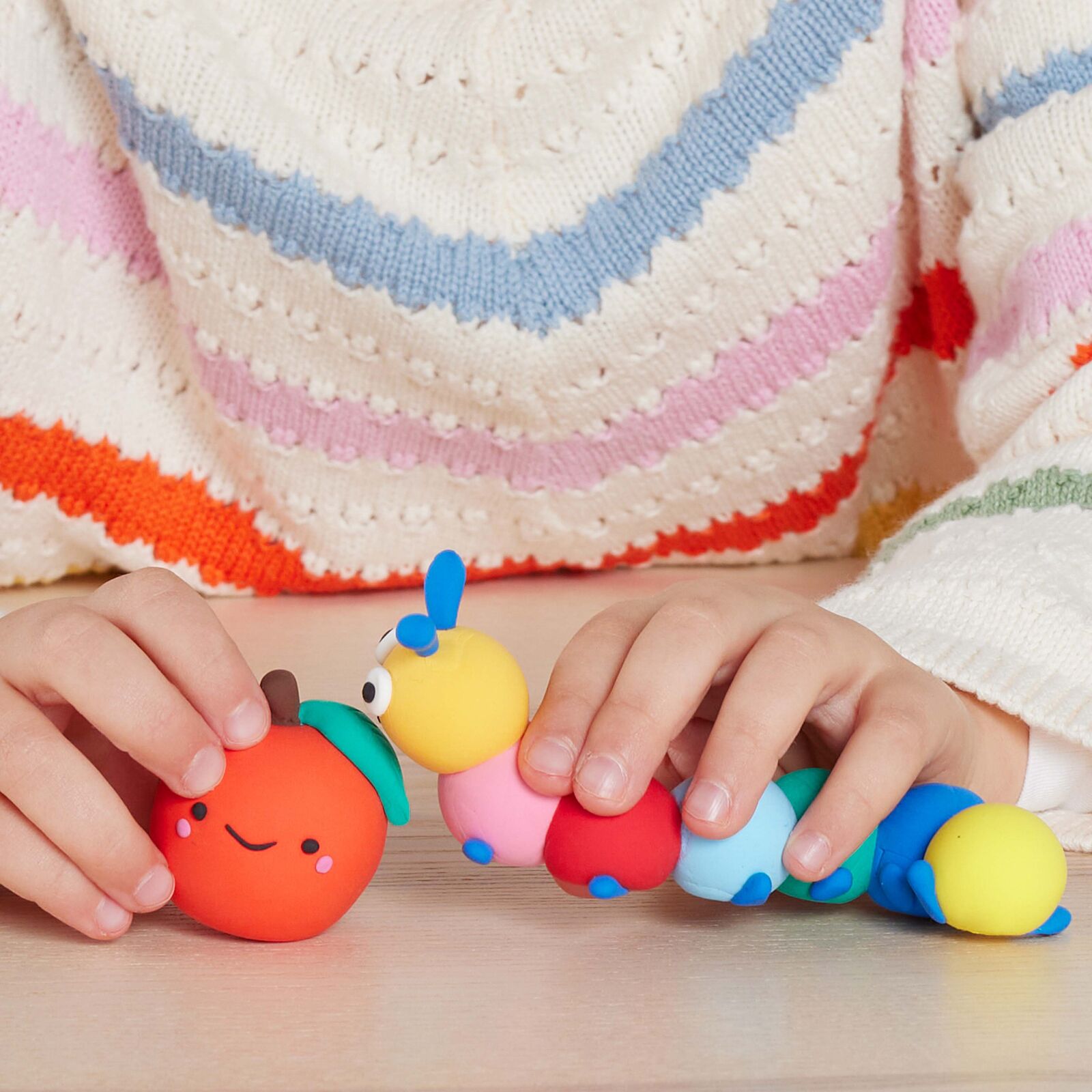 Colorful caterpillar toy held by a child's hands with a striped sweater in the background
