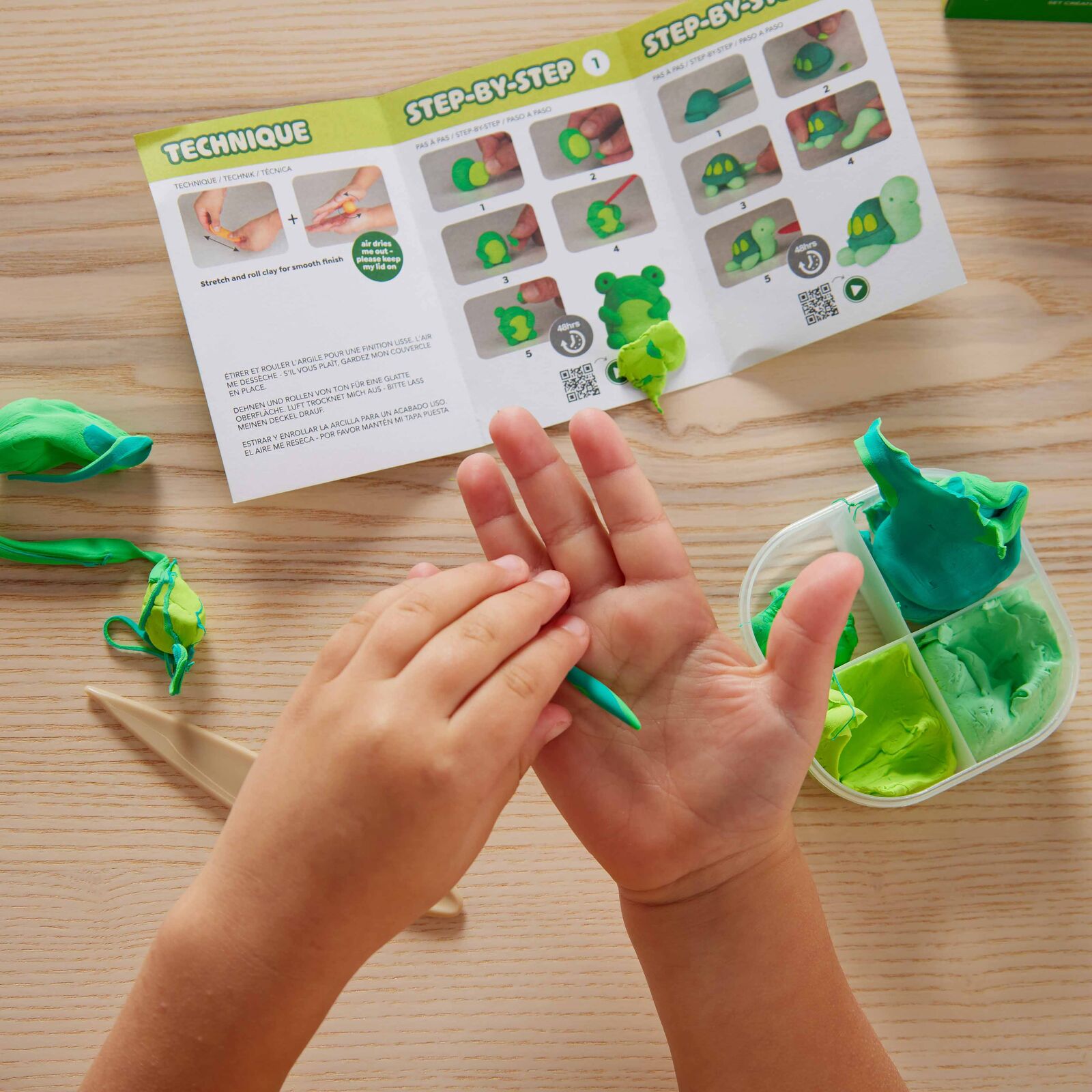 Child's hands working with green clay on a wooden table with a step-by-step guide.