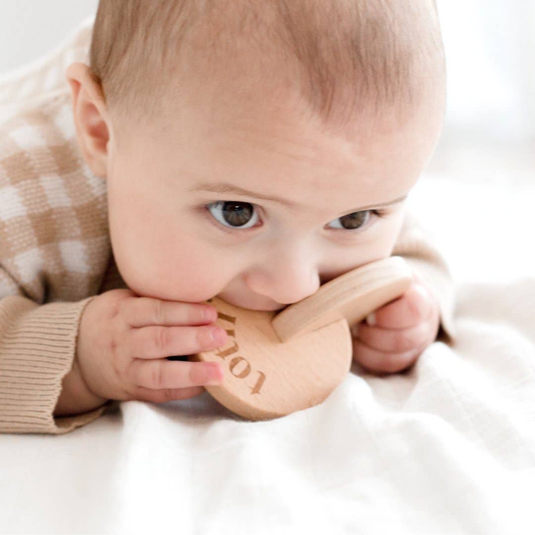 Baby chewing on a wooden teething ring with 'Totli' engraving.