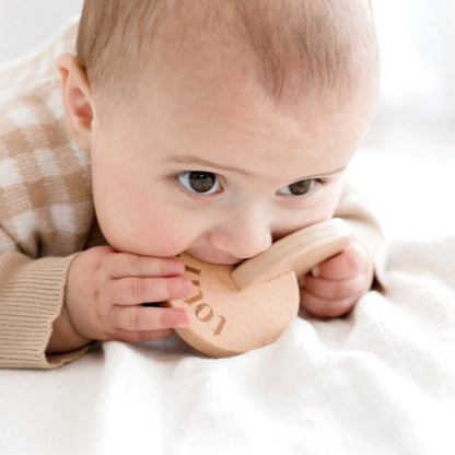 Baby chewing on a wooden teething ring with 'Totli' engraving.