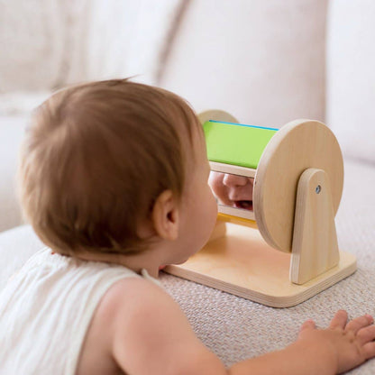 Baby interacting with a wooden toy mirror on a light-colored surface.