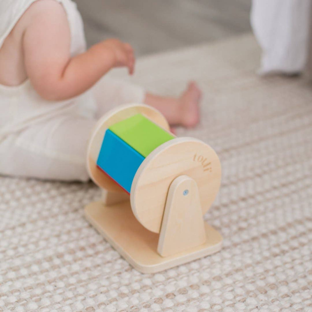 Wooden toy with colorful shapes on a textured surface, likely a carpet.