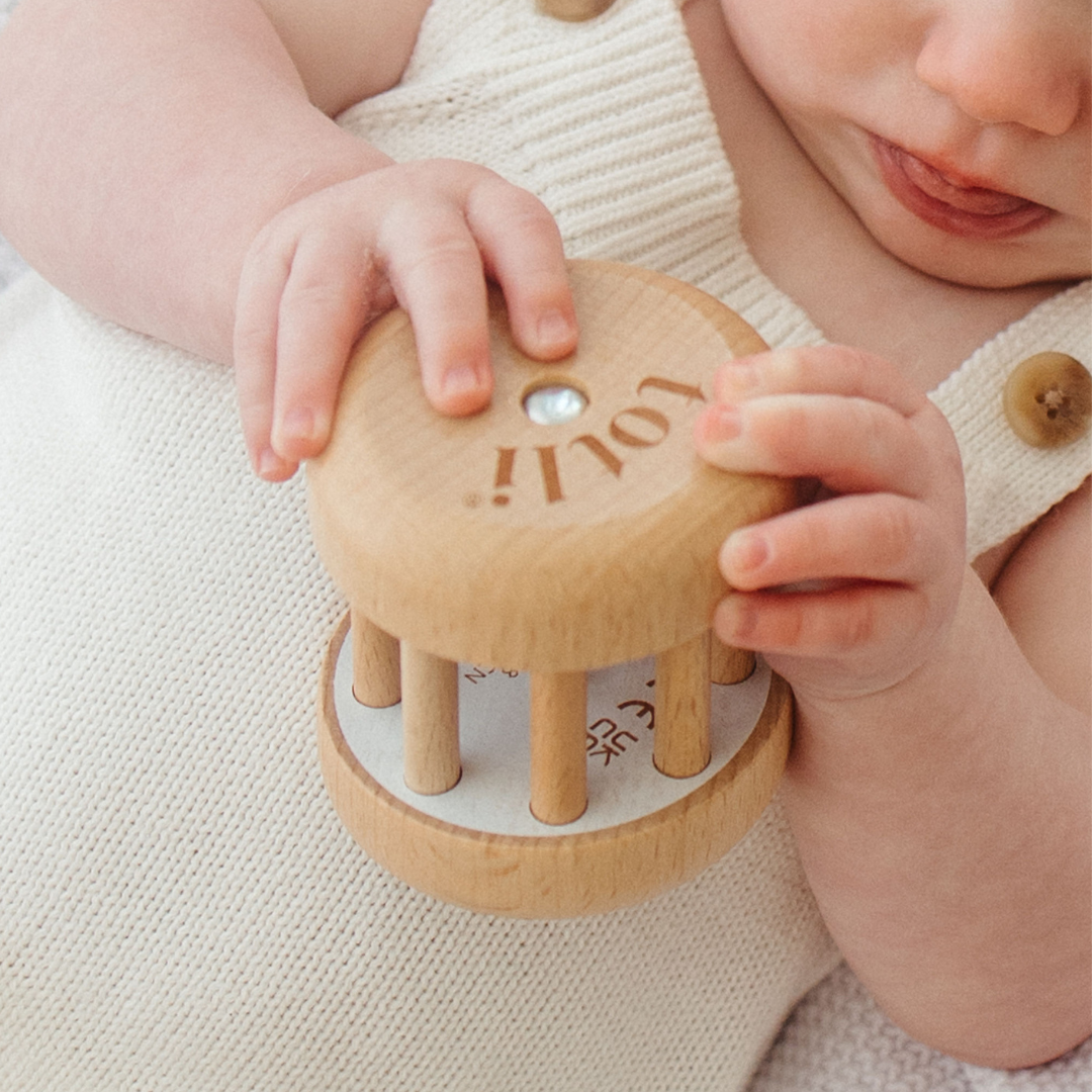 Baby holding a wooden toy with 'Totli' branding