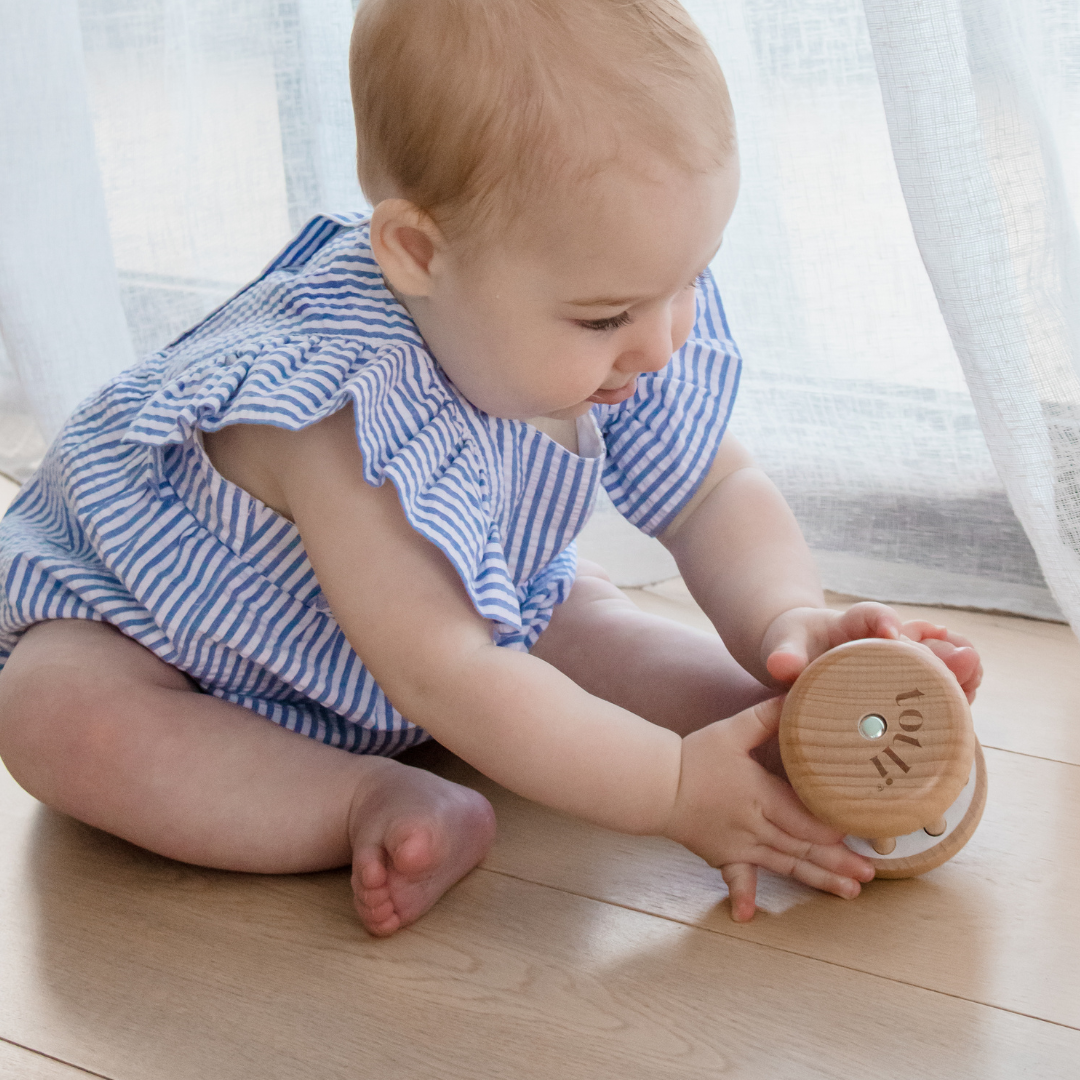 Baby playing with a wooden toy on a wooden floor.