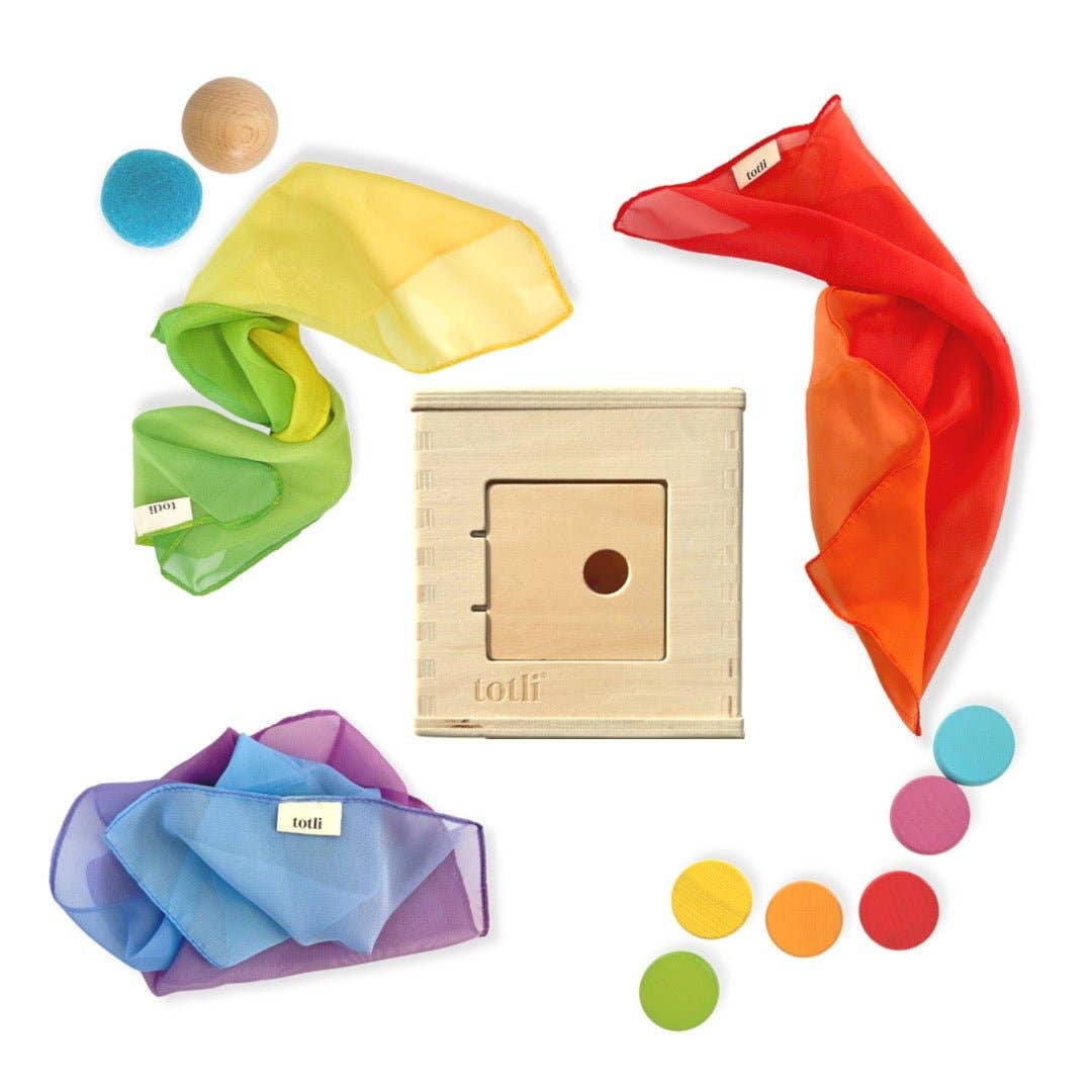 A collection of colorful toys including a wooden box, sensory balls, rainbow coins, and scarves arranged for early childhood play.