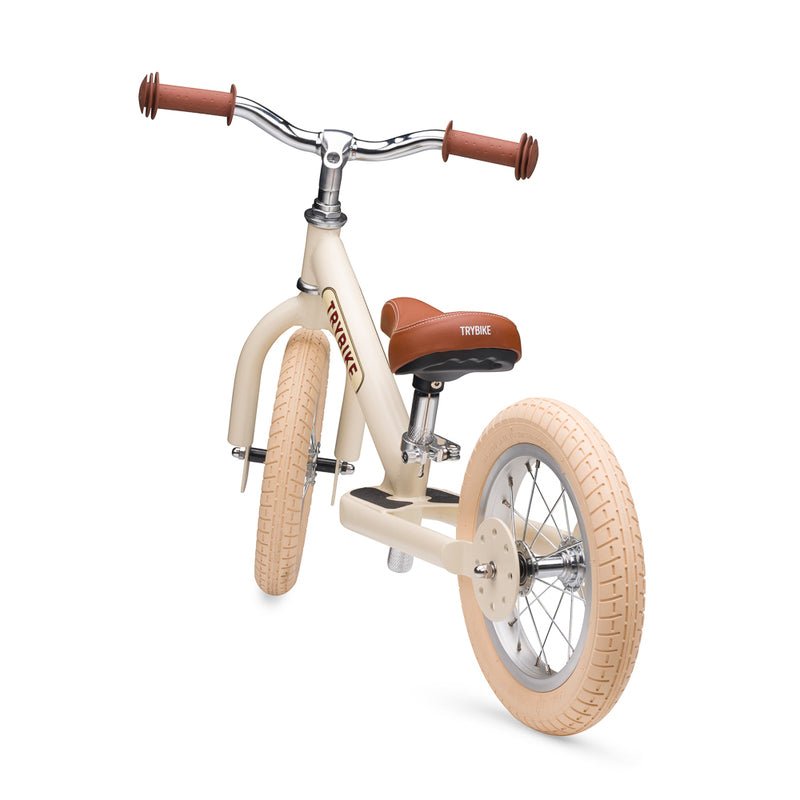 Children's balance bike with cream frame and brown handlebar and seat on a white background