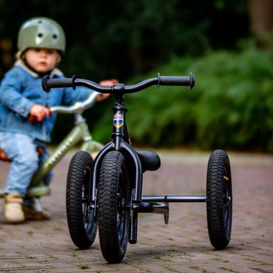 Child riding a balance bike on a paved path with greenery in the background
