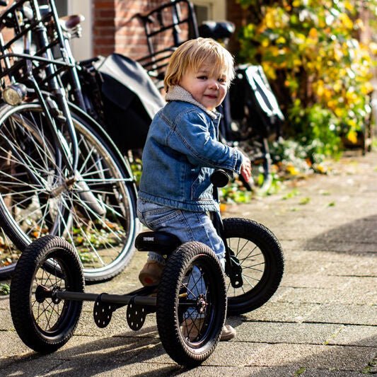 Child on a tricycle in an urban setting with bicycles and buildings in the background