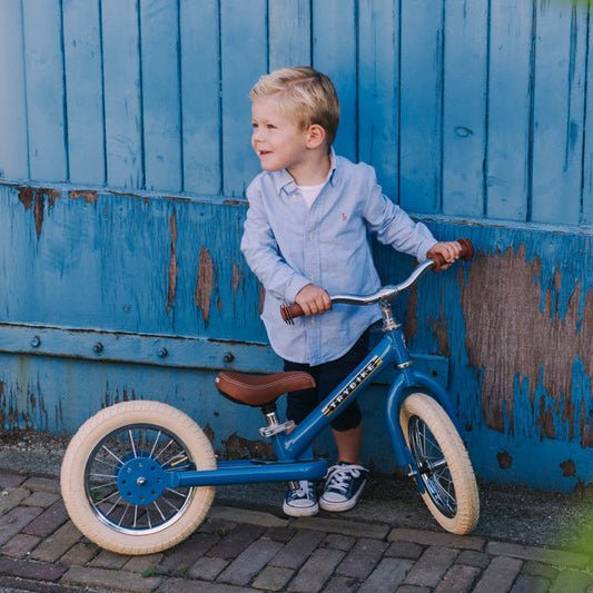 Child with a blue balance bike in front of a blue metal gate.