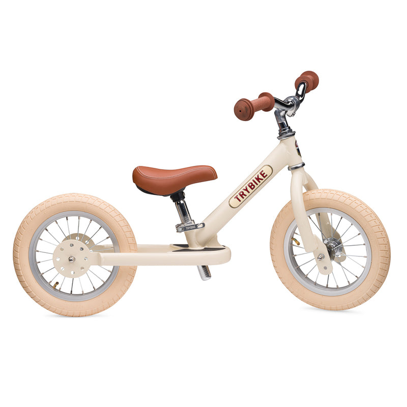Children's balance bike with cream frame and brown seat on a white background