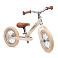 Beige balance bike with brown handlebars and seat on a white background