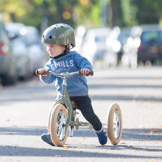 Child riding a balance bike on a street with cars in the background