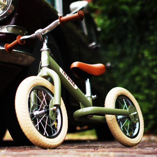 Green balance bike with tan wheels on a wooden surface, blurred background