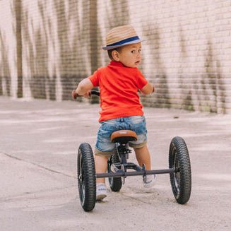 Child riding a tricycle on a sidewalk with a building in the background