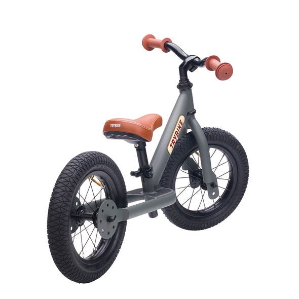 Children's balance bike with black frame, brown seat, and red handlebar grips on a white background