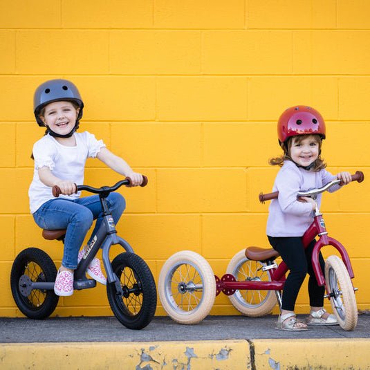 Two children with balance bikes against a yellow wall