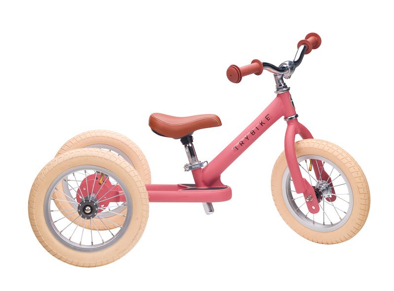 Pink balance bike with tan wheels on a white background