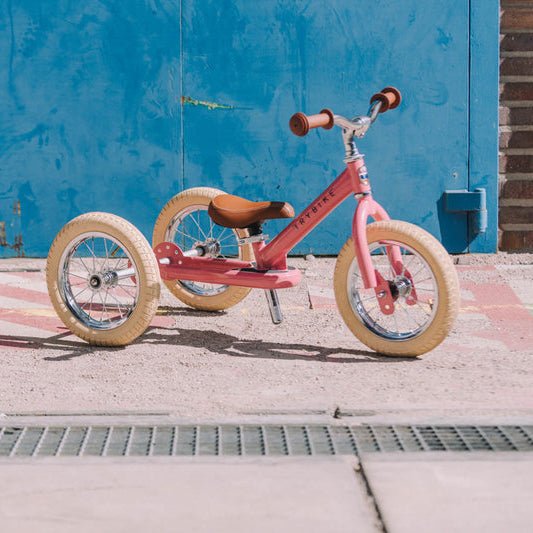 Pink tricycle on a sidewalk with a blue wall in the background