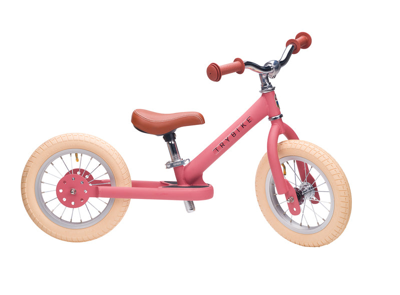 Pink balance bike with wooden wheels on a white background