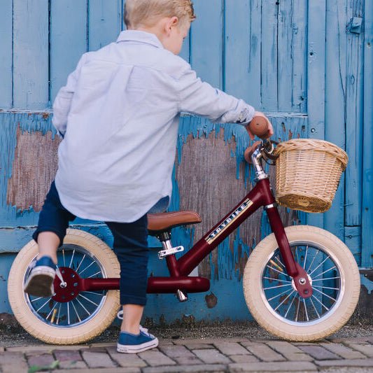 Child on a balance bike with a basket in front of a blue wall