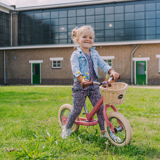 Child on a balance bike in front of a building with green grass