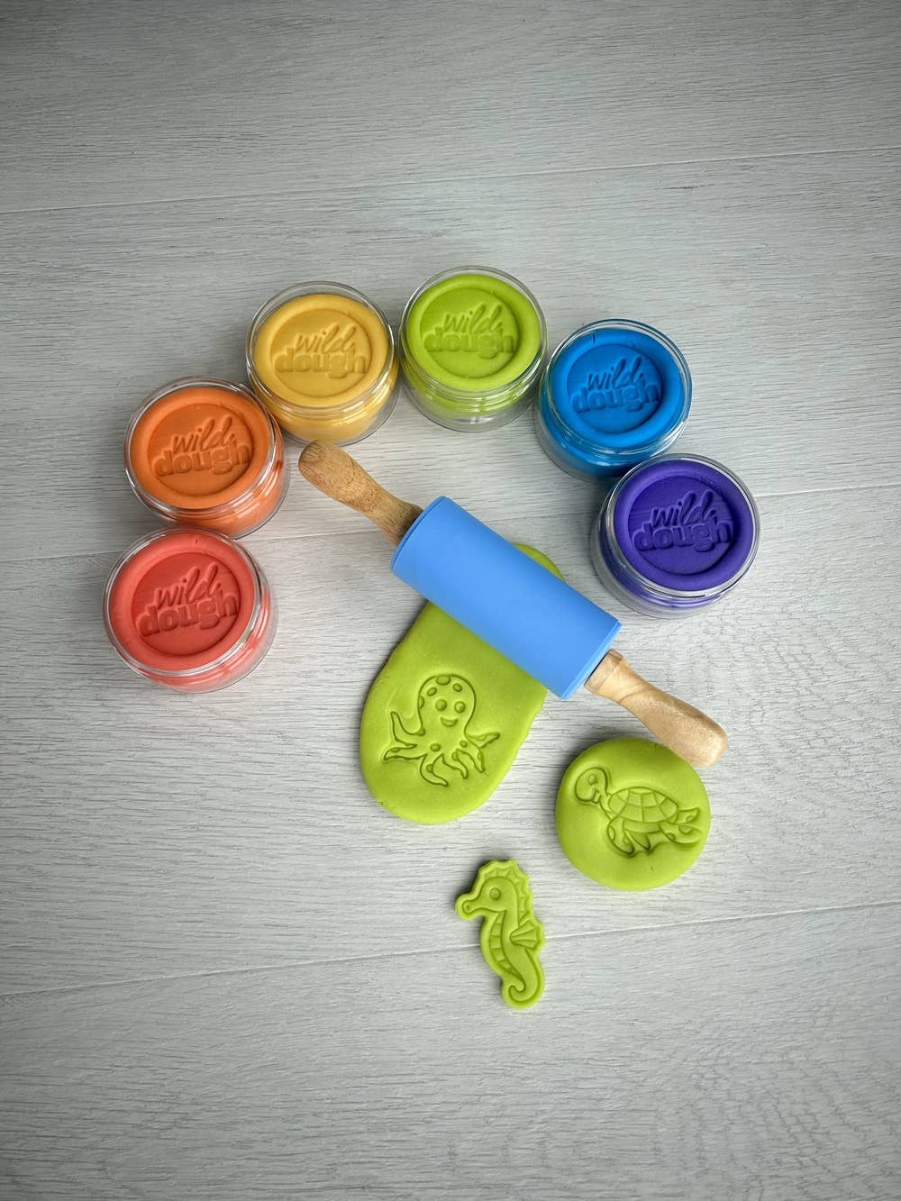 An array of colorful playdough jars with a selection displayed alongside tools for play, all laid out on a light background.