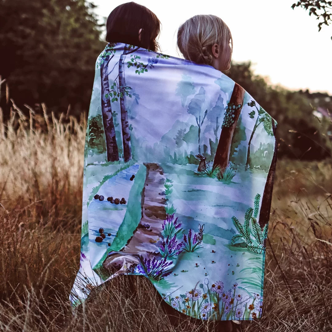 Two people standing in a field with a scenic blanket draped over them