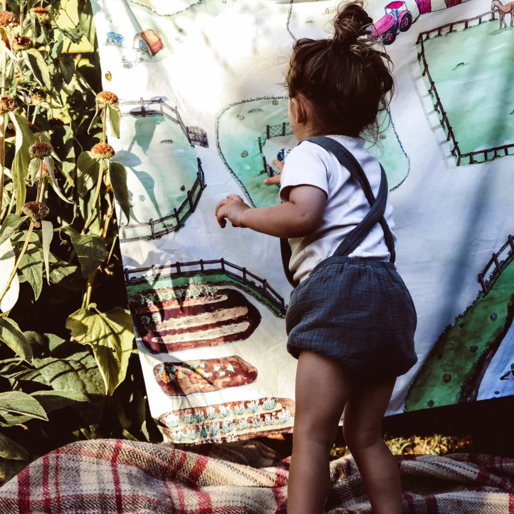 Child playing with a colorful map of a farm in an outdoor setting.