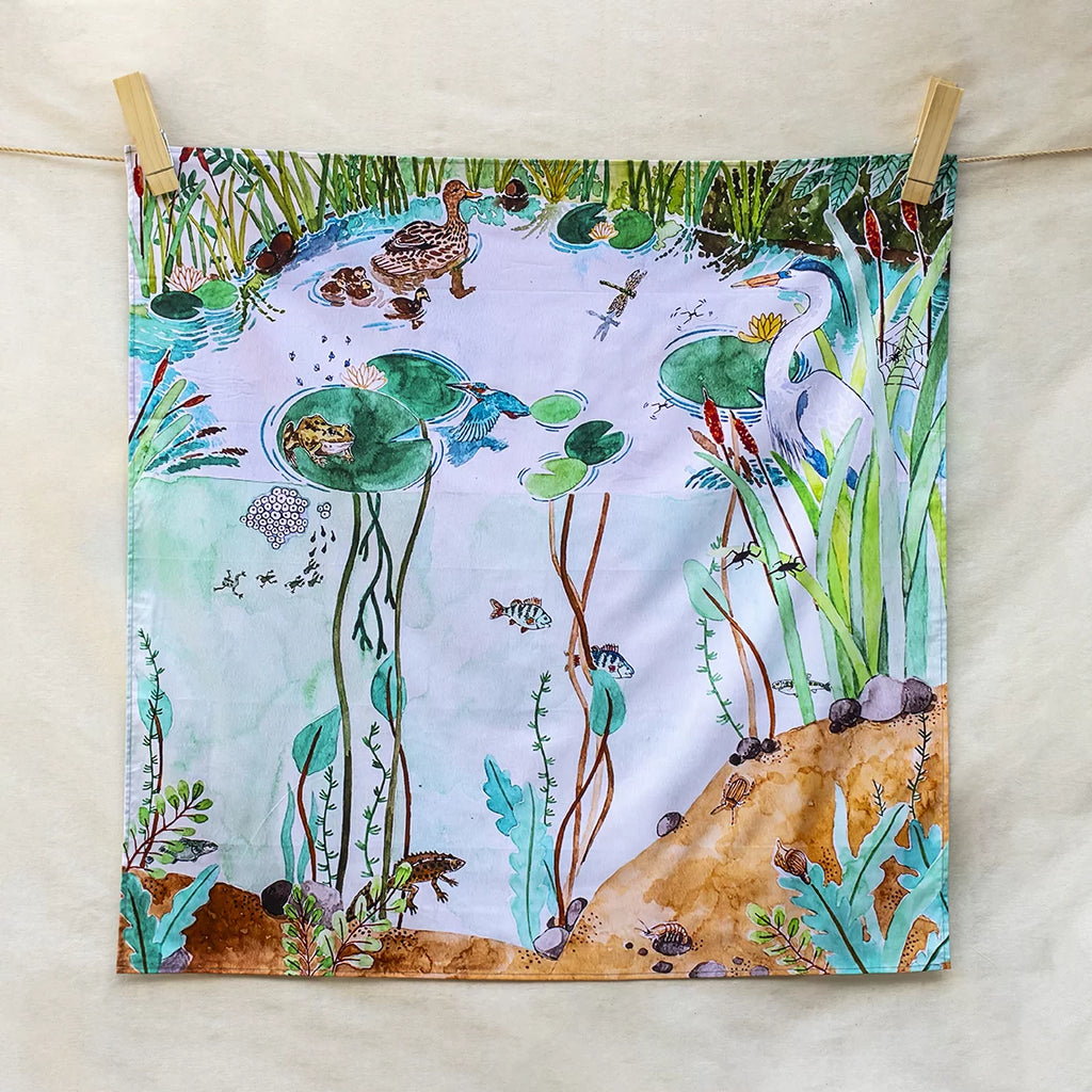 Fabric panel with a nature scene featuring animals and plants, hanging on a line.