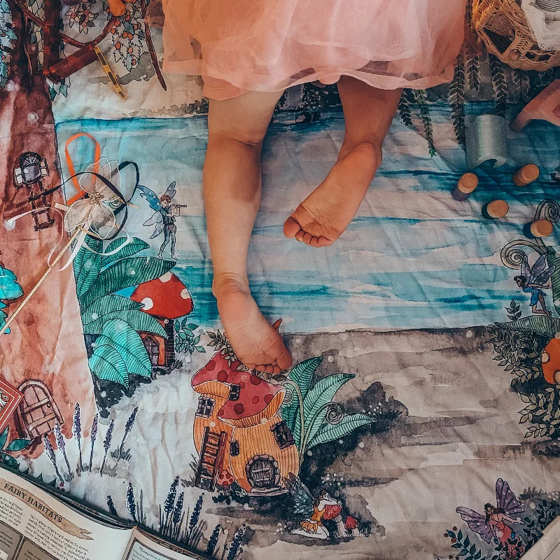 Child's feet standing on a colorful fairy tale-themed rug with mushroom houses and fantasy elements.