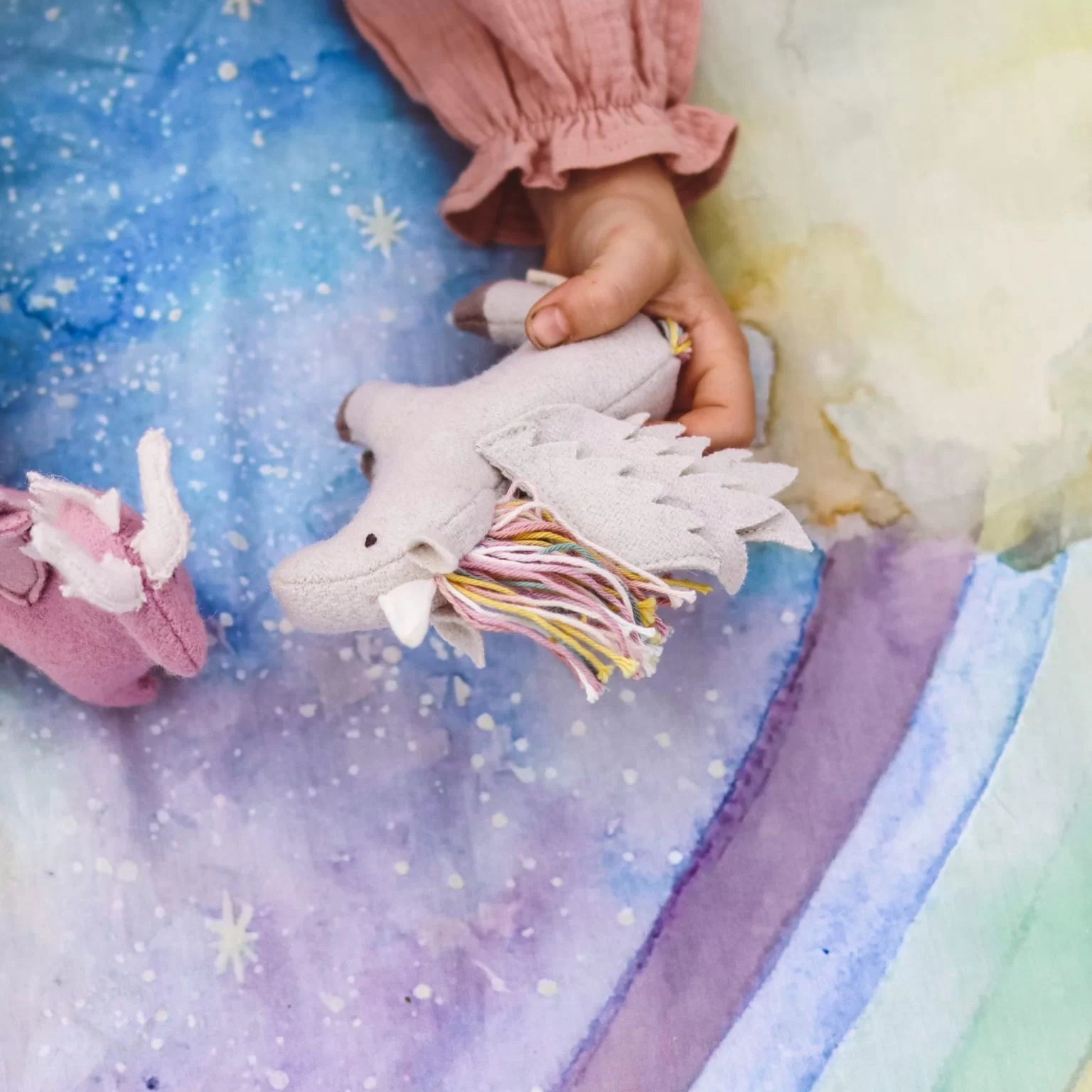 Child's hand holding a unicorn toy on a colorful blanket