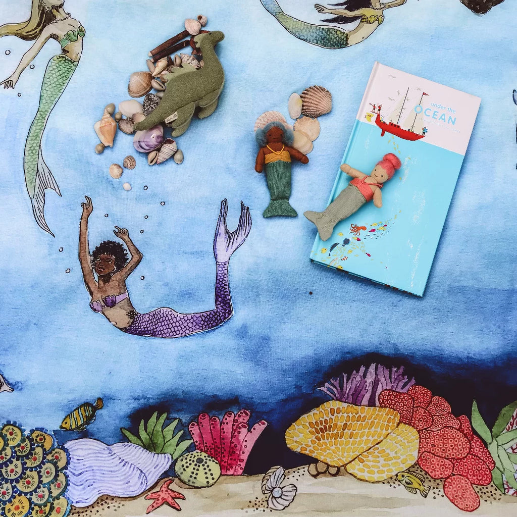 Mermaid-themed playset with toys and a book on a blue watercolor background