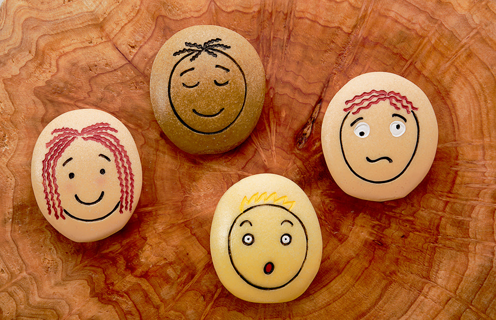 Four stones with faces drawn on them on a wooden surface