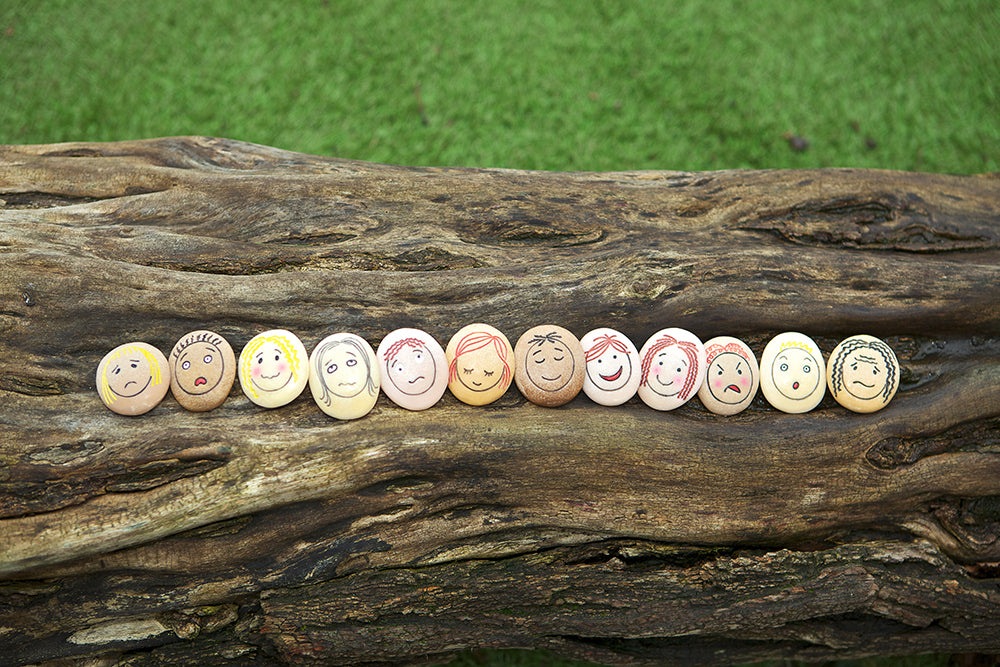 Buttons with smiley faces arranged on a wooden log with a grass background