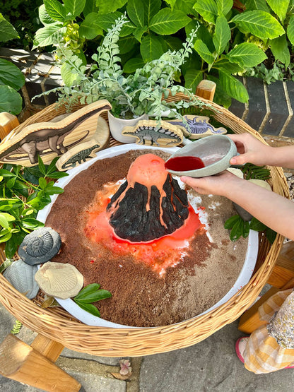 Children's play area with volcano model and sand, surrounded by greenery.