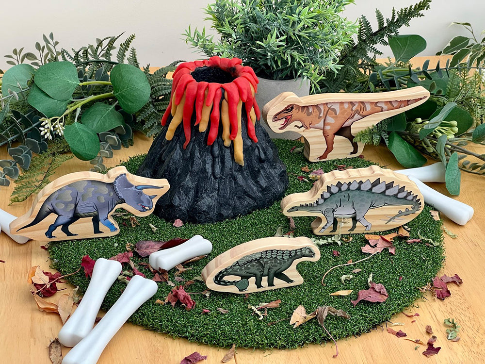 Wooden dinosaur toys with a volcano and greenery on a wooden surface