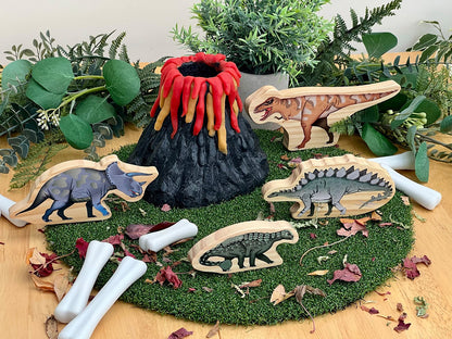 Wooden dinosaur toys with a volcano and greenery on a wooden surface