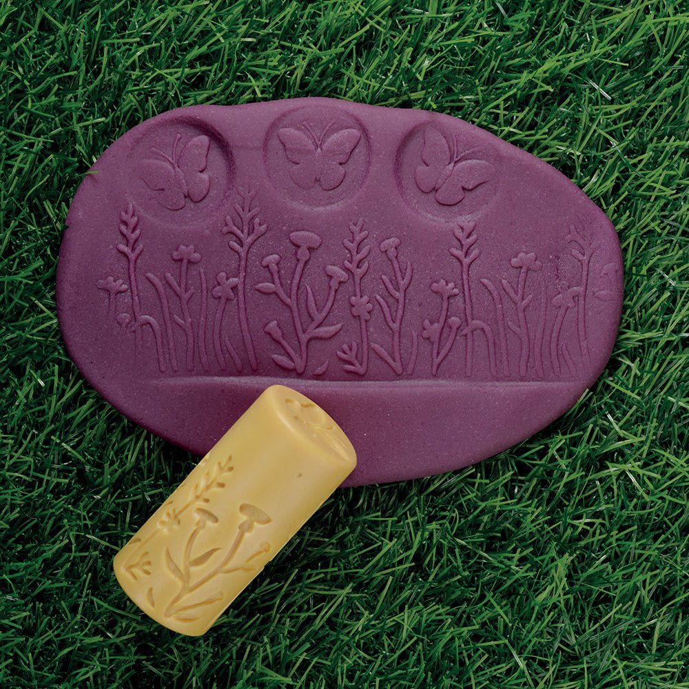 Purple play dough with butterfly roller on grass background.