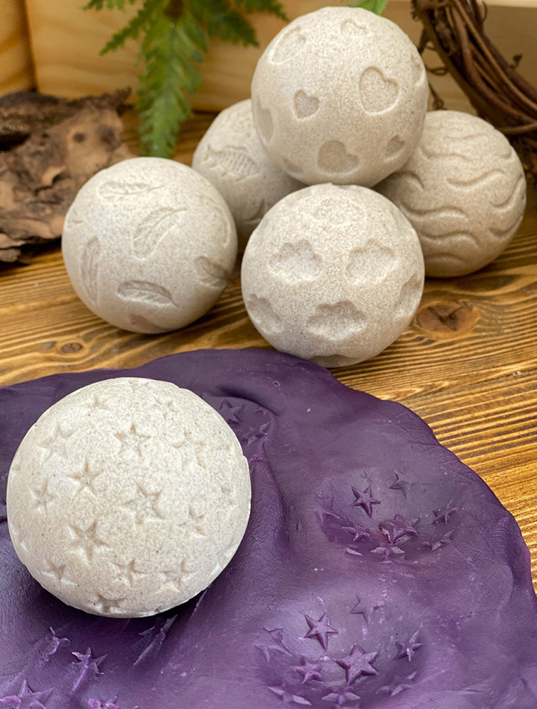 White bath bombs with star patterns on a wooden surface with a purple decorative item.