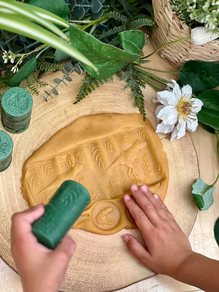 Children's play dough set with a green tool on a textured surface with plants.
