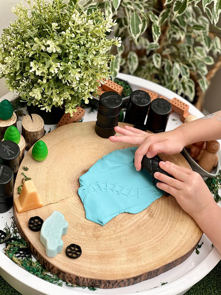 Child playing with play dough on a wooden surface with plants in the background