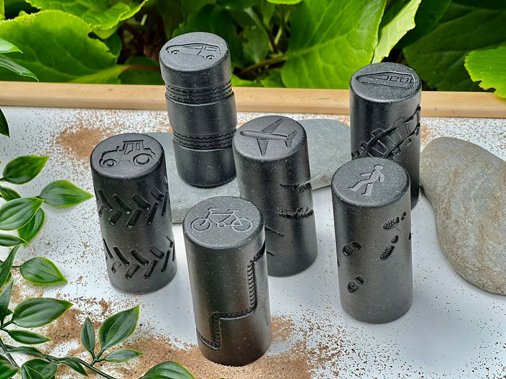 Set of black cylindrical stamps with various symbols on a textured surface with green leaves in the background